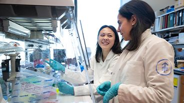Two MSK scientists in lab coats and gloves working and smiling in a laboratory.